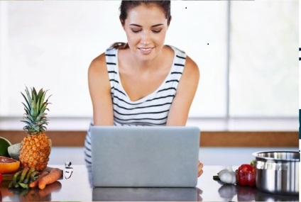Mujer sonriente cortando frutas y verduras en cocina moderna mientras usa laptop